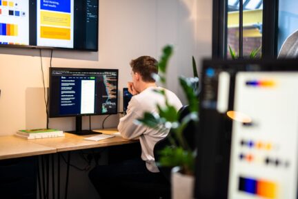 Man sat at computer developing code for web application in an office.